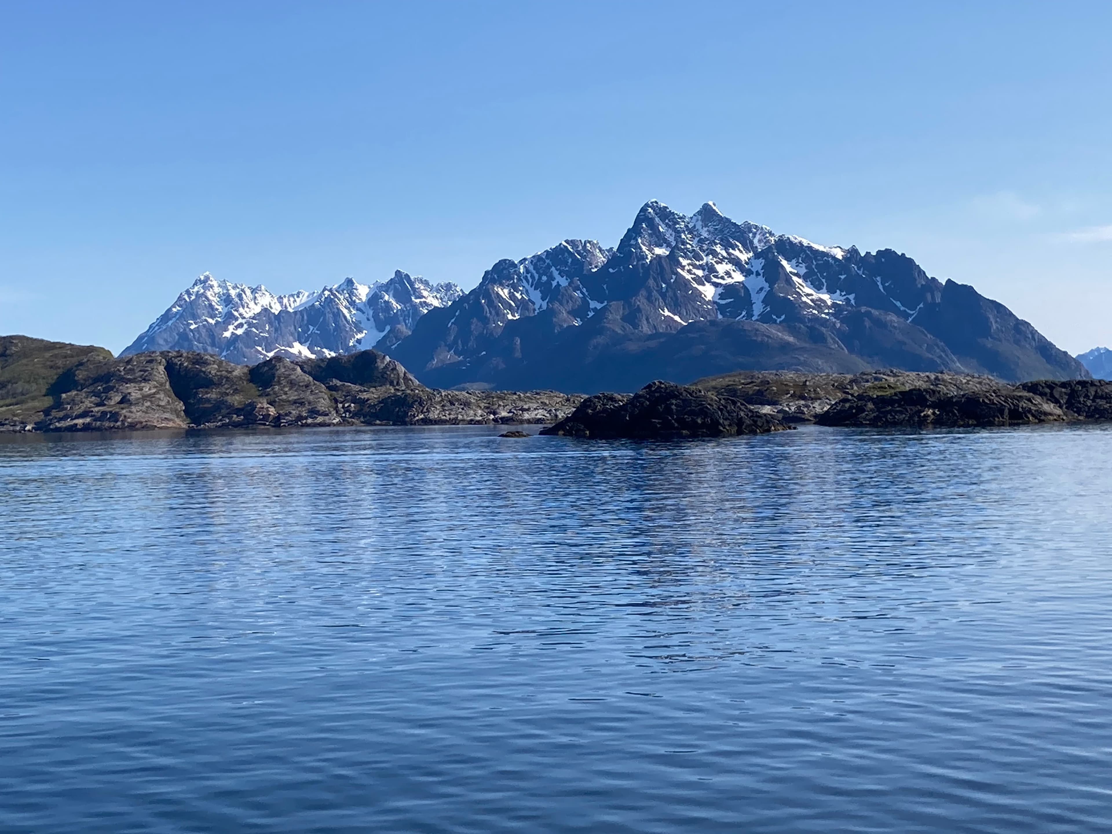 Snow-capped mountains rising behind low rocky islands across calm blue water