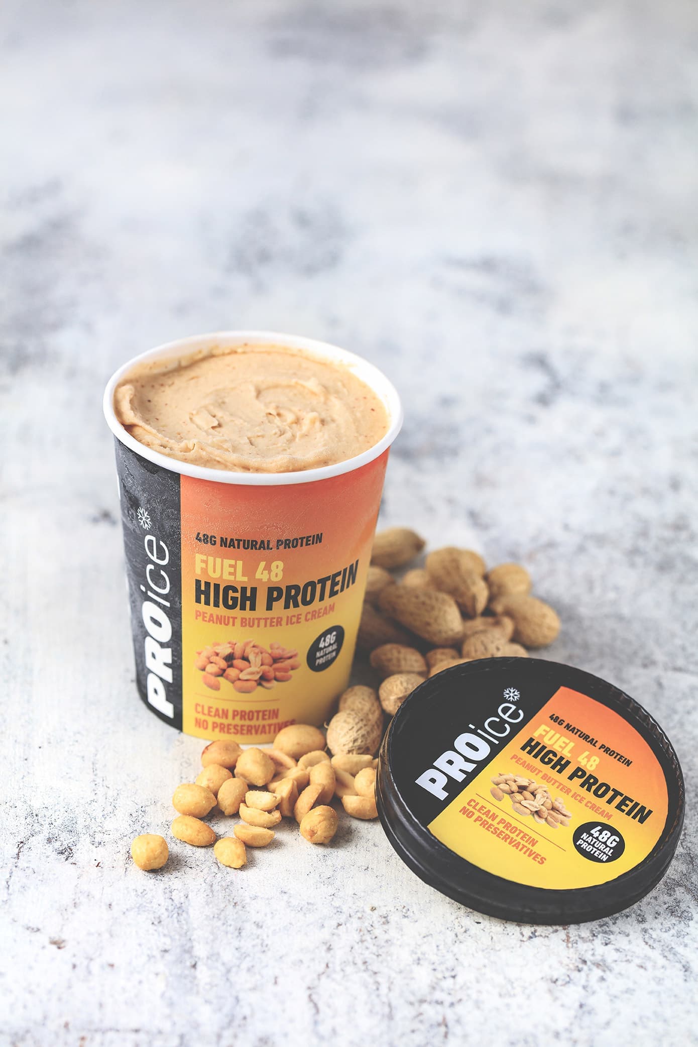 An open tub of PROice Fuel 48 High Protein Peanut Butter Ice Cream with peanuts