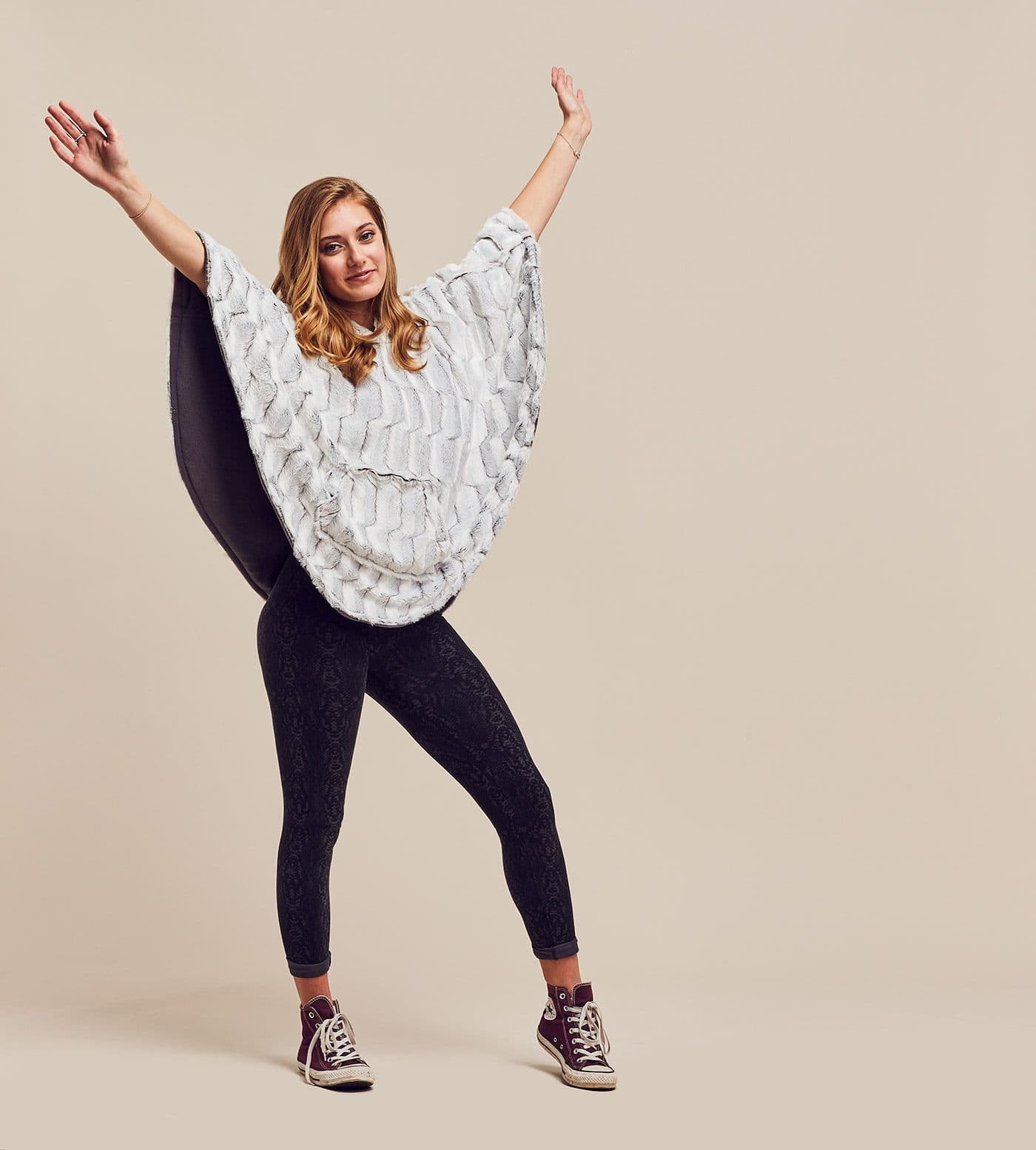 A woman in a grey patterned Ponchella poncho with her arms raised