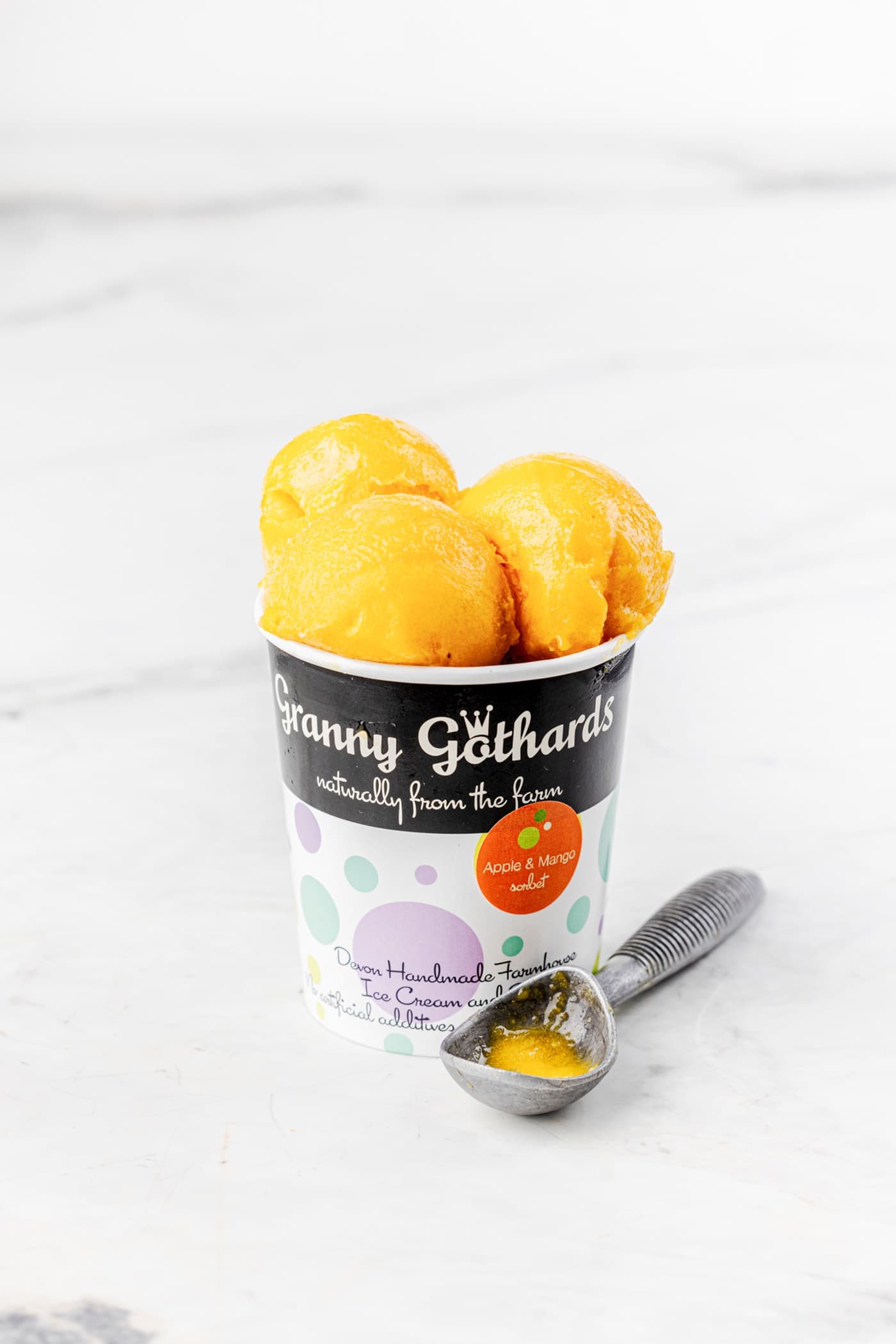 A Granny Gothards pot filled with orange sorbet, with a scoop beside it
