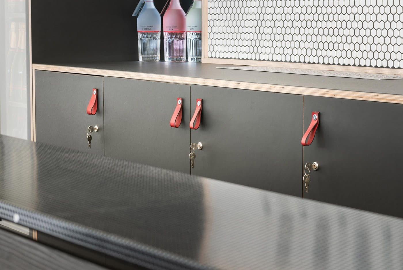 A dark bar counter with red leather pull handles, bottles and a hexagon tiled back wall