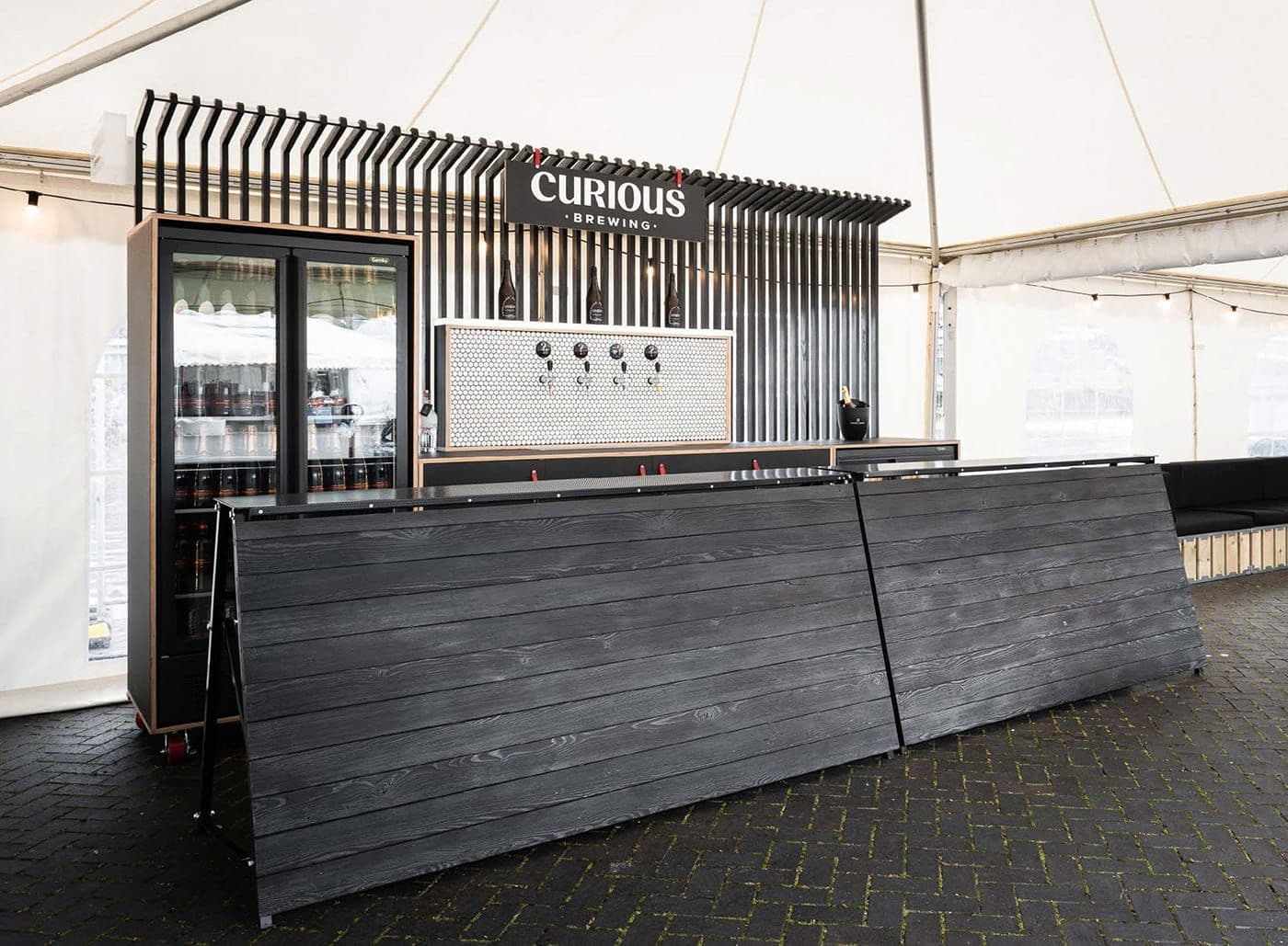 The Curious Brewing bar inside a marquee, with a slatted timber counter and branded fascia