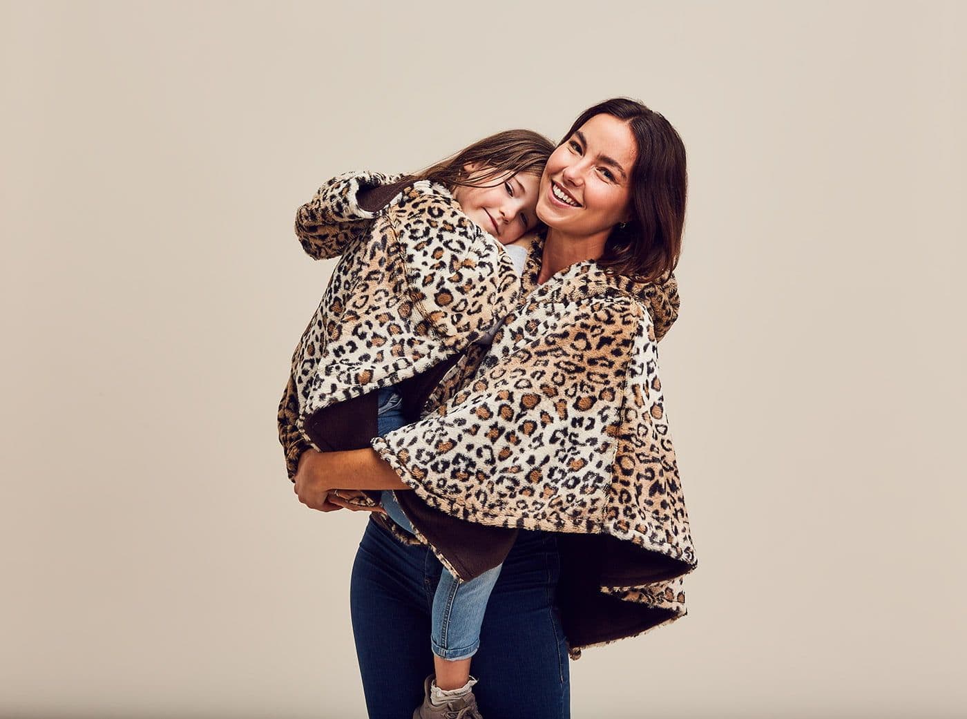 A smiling mother carrying her daughter, both wearing leopard print Ponchella ponchos