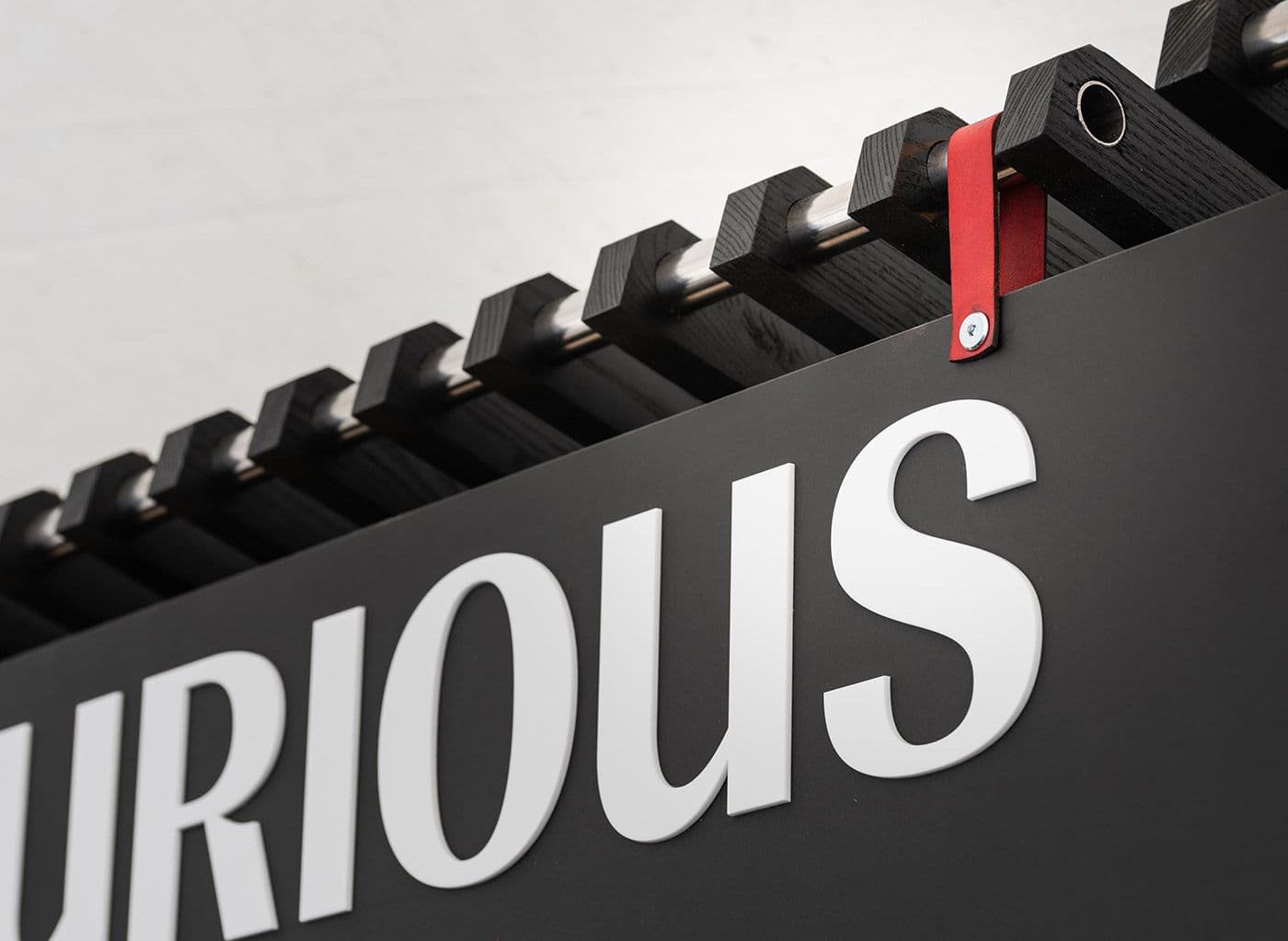 Close-up of the Curious lettering on the bar fascia, with slatted timber and a red leather strap