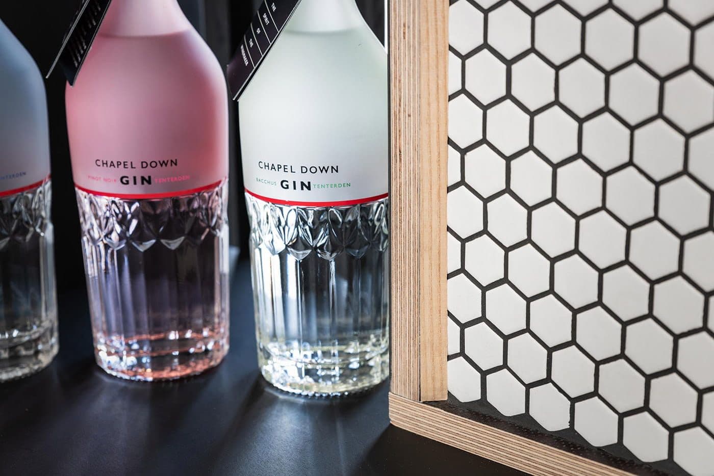 Chapel Down gin bottles on a bar beside a white hexagon tiled wall