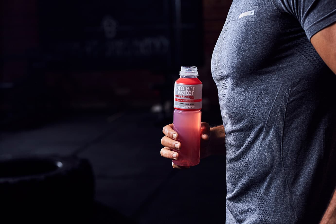 Close-up of a bottle of raspberry Protein Water held at an athlete's side