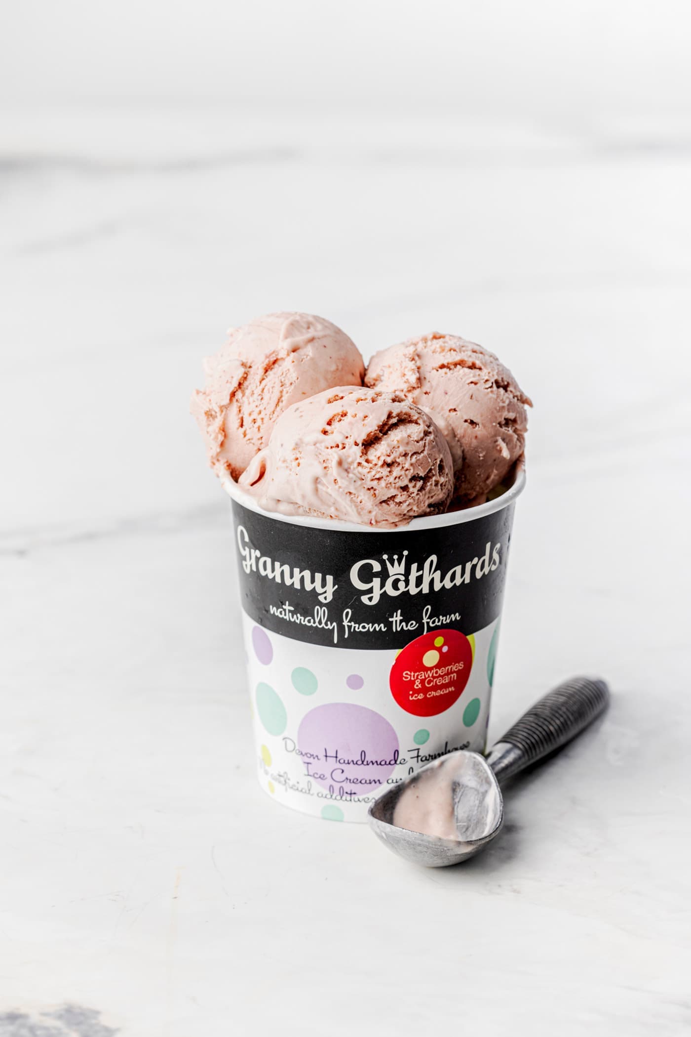 A Granny Gothards ice cream pot filled with scoops of pink ice cream, with a scoop beside it
