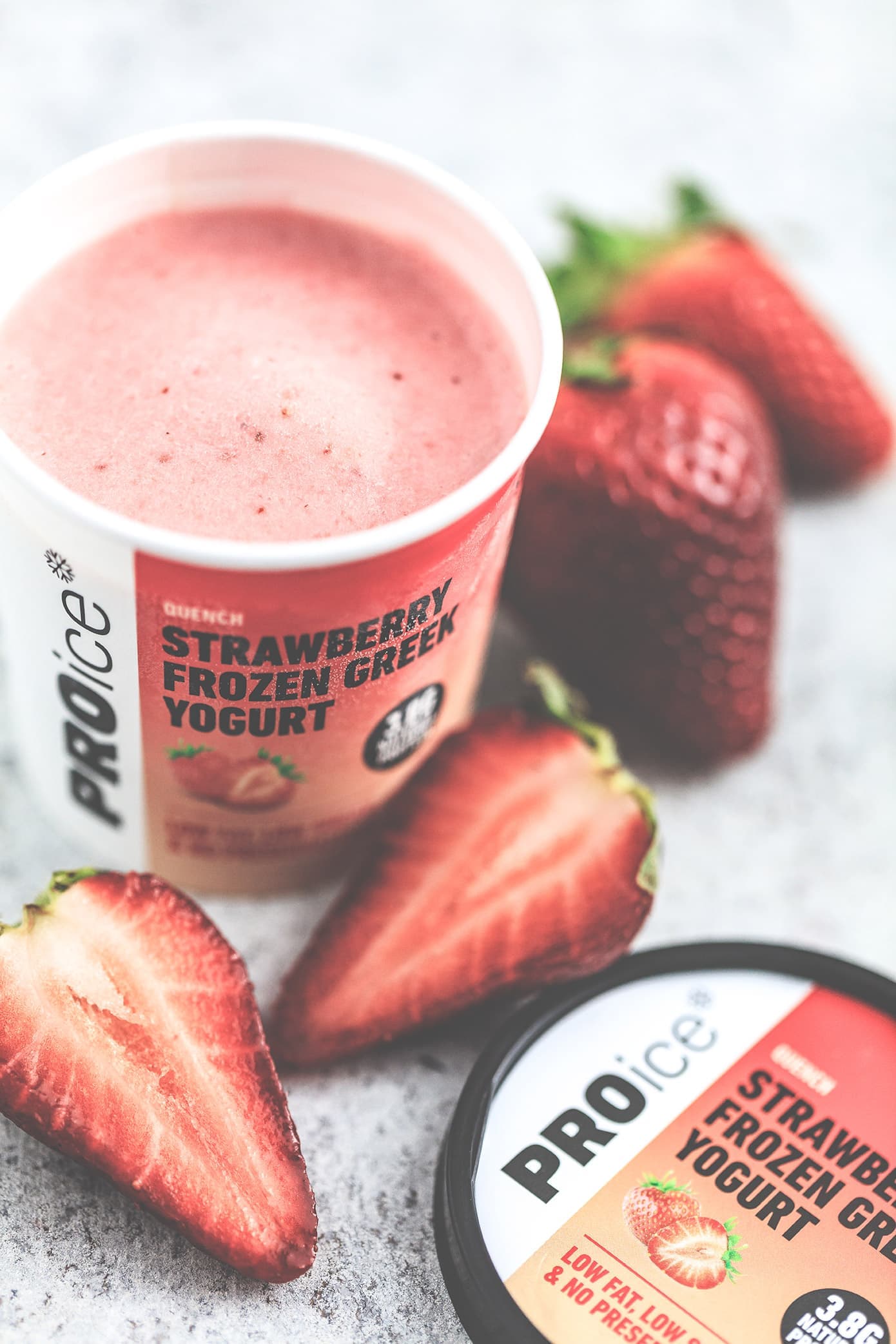 Close-up of an open tub of PROice Strawberry Frozen Greek Yogurt with halved strawberries
