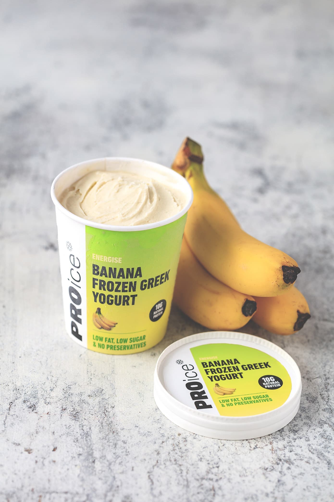 An open tub of PROice Banana Frozen Greek Yogurt with bananas