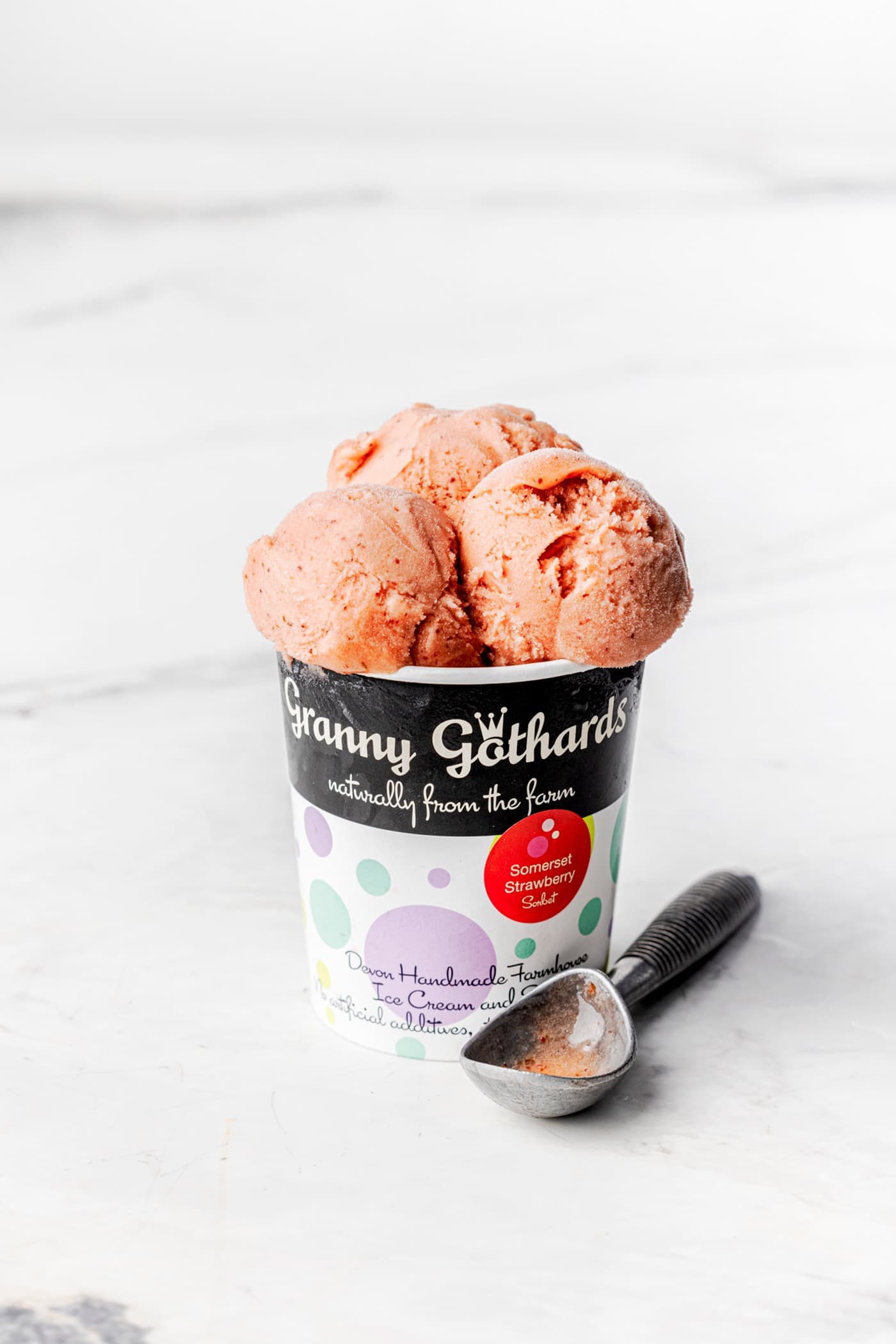 A Granny Gothards pot filled with strawberry ice cream, with a scoop beside it